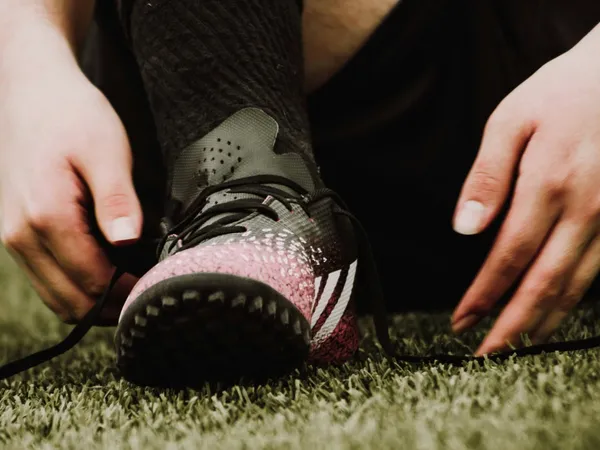 Person lacing up a football boot on grass