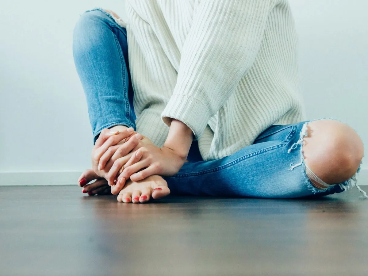 Person sitting on the floor holding their bare feet